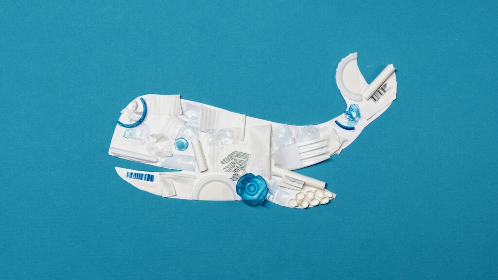 Eco-friendly concept art of a whale crafted from white plastic waste on a blue background.