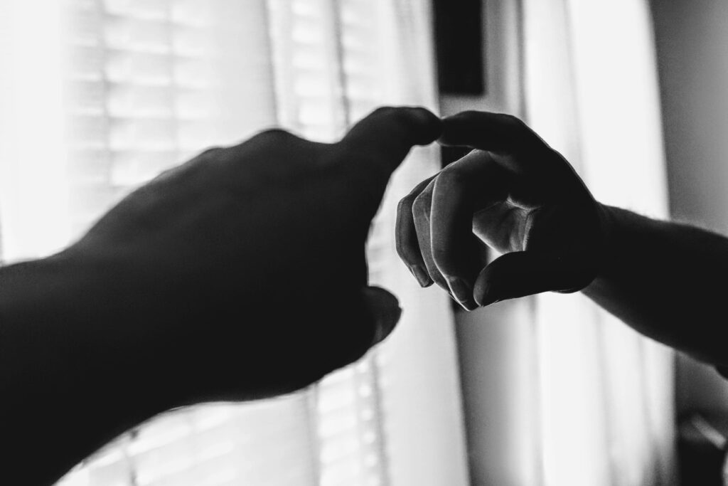 A dramatic black and white photo of a hand reaching toward a mirror, creating a reflective illusion.