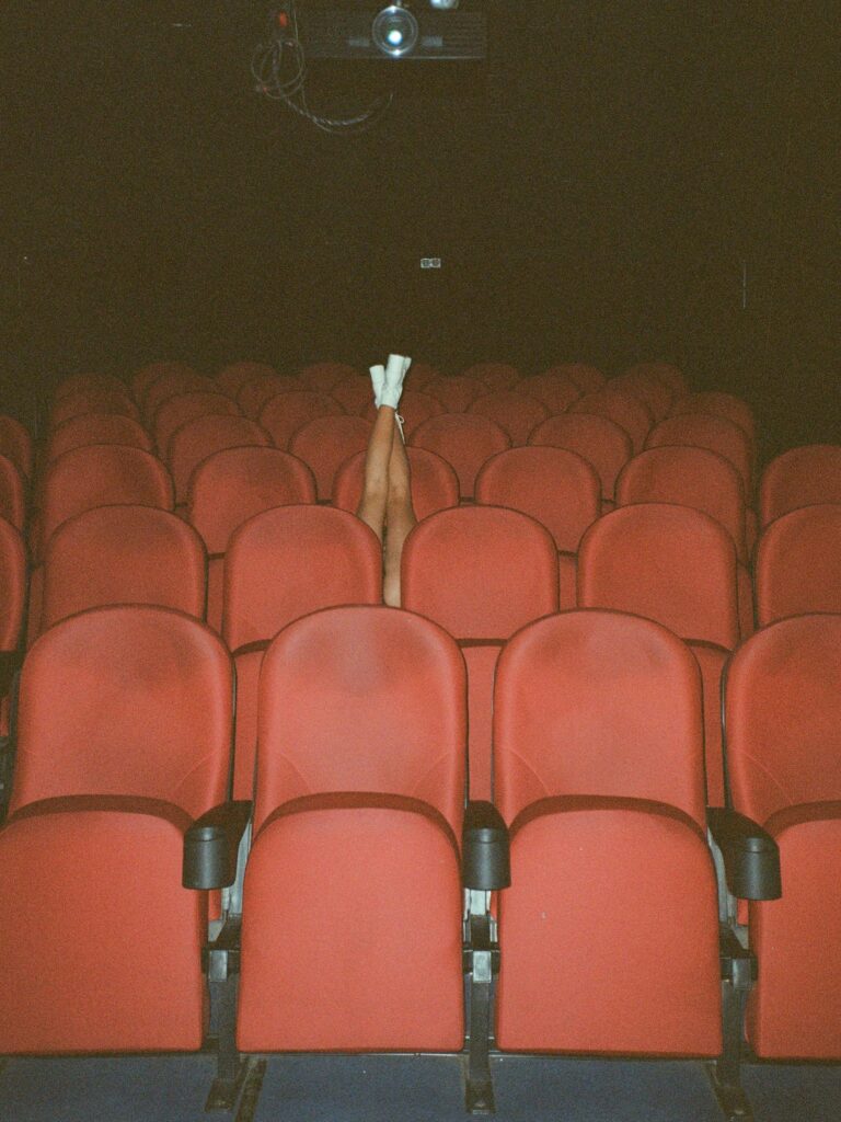Legs raised among empty red theater seats creating a whimsical scene.