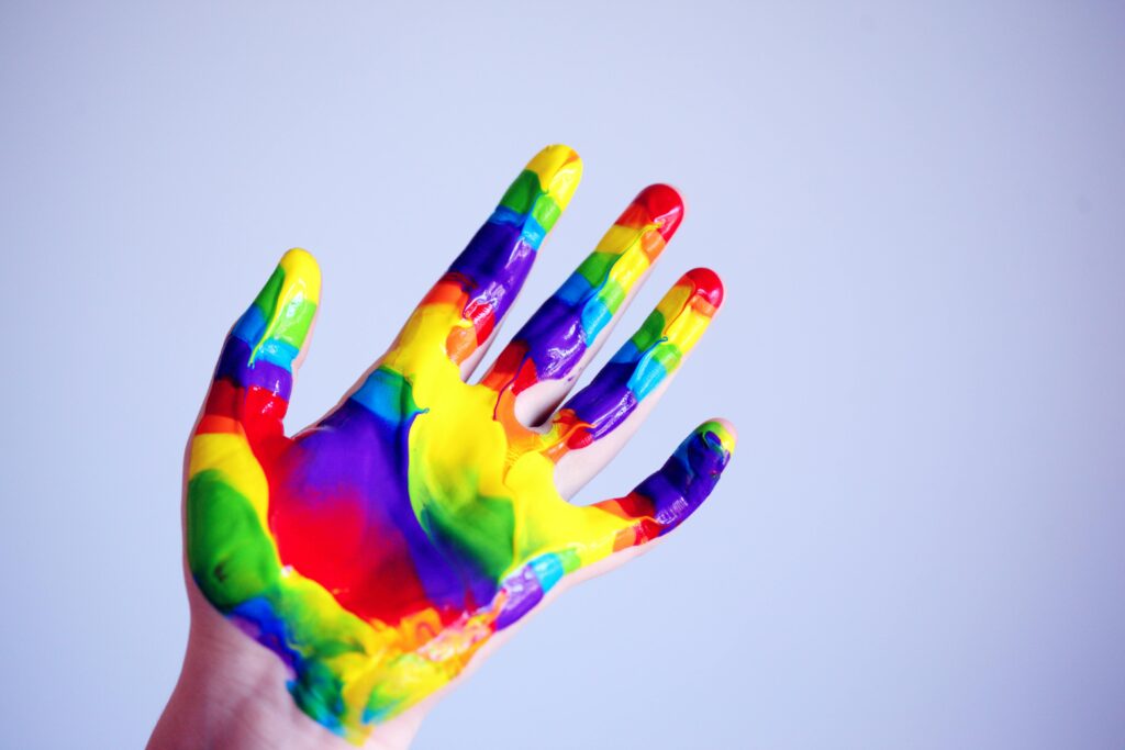A vibrant hand covered in rainbow paint against a plain background, symbolizing creativity.