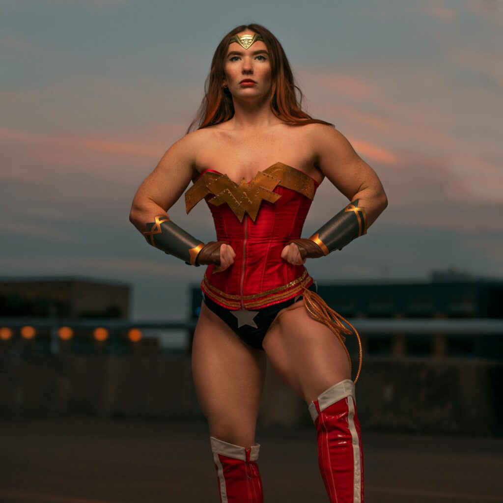 A strong woman dressed as a superhero posing with confidence outdoors during sunset.