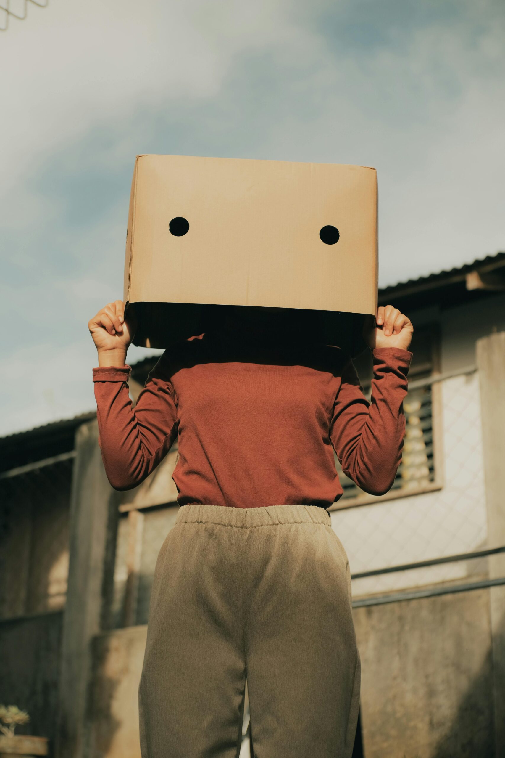A person wearing a cardboard box on their head, posing anonymously outdoors.